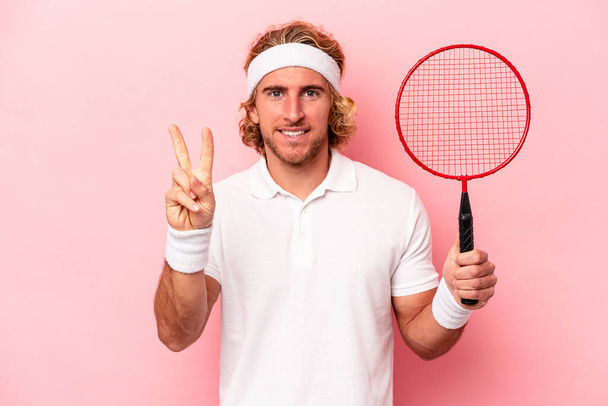 Junger kaukasischer Mann spielt Badminton isoliert auf rosa Hintergrund und zeigt Nummer zwei mit Fingern. - Foto, Bild
