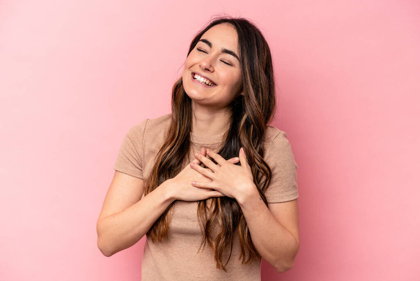 Young caucasian woman isolated on pink background laughing keeping hands on heart, concept of happiness. - Photo, Image