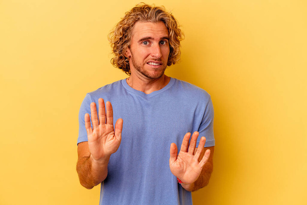 Young caucasian man isolated on yellow background rejecting someone showing a gesture of disgust. - Photo, Image