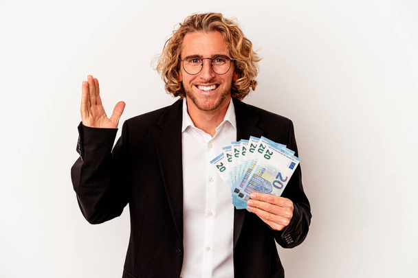 Fiatal kaukázusi üzletember kezében bankjegyek elszigetelt fehér alapon kap egy kellemes meglepetés, izgatott és felemeli a kezét. - Fotó, kép