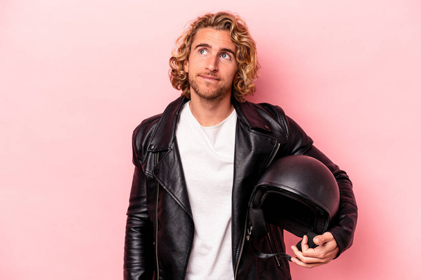 Young caucasian man with a motorcycle helmet isolated on pink background dreaming of achieving goals and purposes - 写真・画像