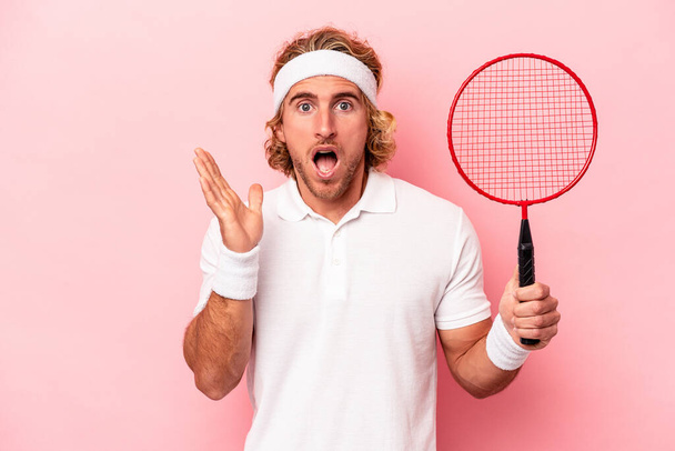 Young caucasian man playing badminton isolated on pink background surprised and shocked. - Photo, Image