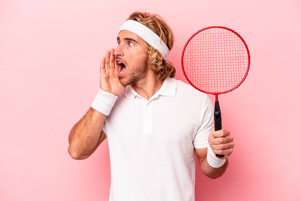 Young caucasian man playing badminton isolated on pink background shouting and holding palm near opened mouth. - Photo, Image