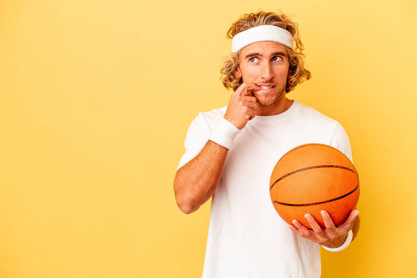 Young basketball player caucasian man isolated on yellow background relaxed thinking about something looking at a copy space. - Photo, Image