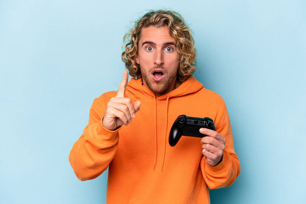 Young caucasian man playing with a video game controller isolated on blue background having an idea, inspiration concept. - Foto, Imagem