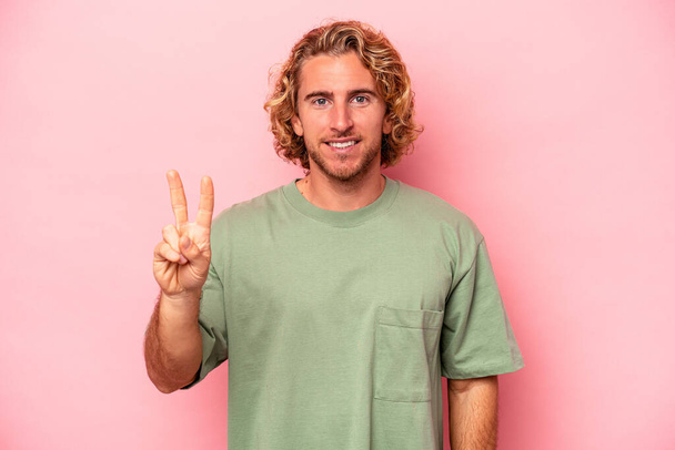 Young caucasian man isolated on pink background joyful and carefree showing a peace symbol with fingers. - Photo, Image