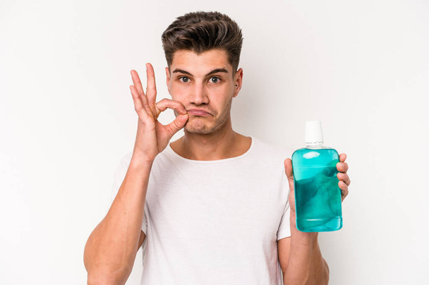 Young caucasian man holding mouthwash isolated on white background with fingers on lips keeping a secret. - Zdjęcie, obraz