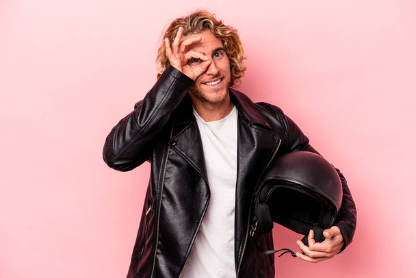 Young caucasian man with a motorcycle helmet isolated on pink background excited keeping ok gesture on eye. - Foto, immagini