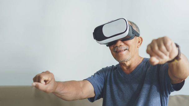 Happy Asian Senior Adult is using VR glasses headset with virtual reality motorcycle game at home. - 写真・画像