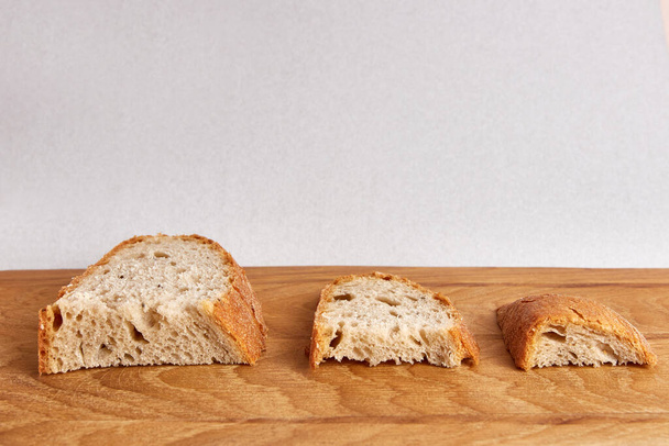 Τρία κομμάτια ψωμί μεγαλύτερα, μικρότερα και ακόμα μικρότερα σε μια ξύλινη σανίδα. Η έννοια της επισιτιστικής κρίσης του 2022 και του 2023. - Φωτογραφία, εικόνα