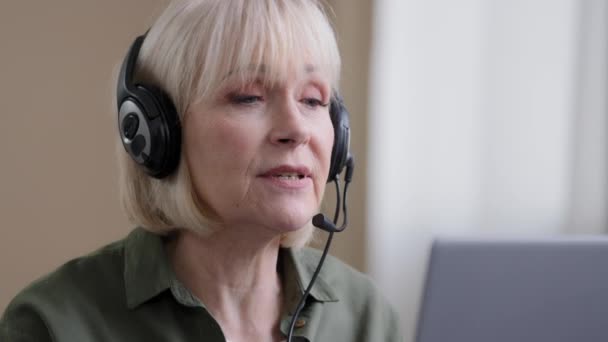 Close up senior Caucasian wrinkled businesswoman mature lady online teacher in headset class lesson remote from home client help distant. Elderly serious grandmother talking laptop webcam with doctor - Video