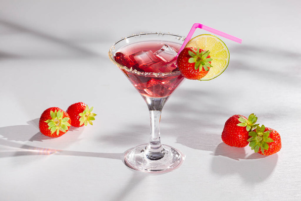 Delicious cocktail. Red sweet cold party drink in elegant shot glass with ice cubes, strawberry and lime on white table - Φωτογραφία, εικόνα