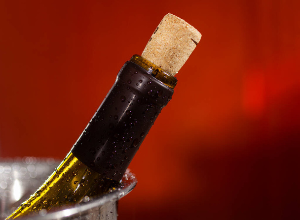 Close up of neck of a wine bottle with a cork in drops of water on red background - Foto, Imagen