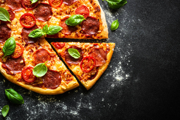 Pizza z serem salami, pomidorami i bazylią na czarnym stole. Widok z góry z przestrzenią do kopiowania, makro. - Zdjęcie, obraz