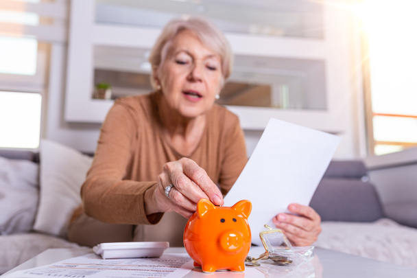 Tasarruf, para, yıllık sigorta, emeklilik ve yaşlı kadın kumbarasına para koyuyor. Mutlu Olgun Kadın Kumbarada Para Hesaplıyor - Fotoğraf, Görsel