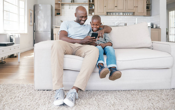 Shot of a father and son using a cellphone on the sofa at home. - Foto, imagen