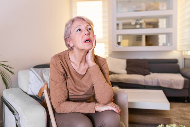Mature woman holding her head with her hands while having a headache and feeling unwell. Senior woman with headache, pain face expression. Elderly woman having head pain migraine - Foto, Bild