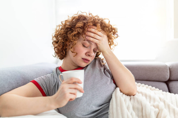 Przygnębiona kobieta leżąca na biurku z filiżanką kawy w dłoni, przygnębiona młoda kobieta leżąca na kanapie czująca ból głowy migrena, smutna, zmęczona, zmęczona nastolatka wyczerpana dziewczyna jest zdenerwowana i zestresowana - Zdjęcie, obraz