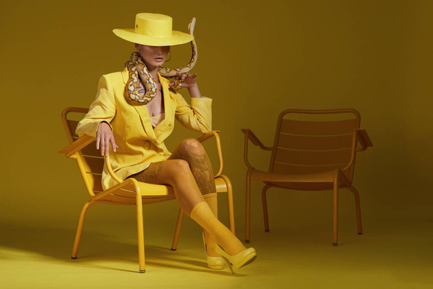 Girato di una donna alla moda che tiene un serpente mentre modella un concetto giallo. - Foto, immagini