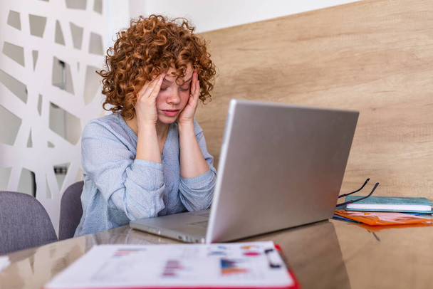 Young frustrated woman working at office desk in front of laptop suffering from chronic daily headaches, treatment online, appointing to a medical consultation, electromagnetic radiation, sick pay - Foto, Imagem