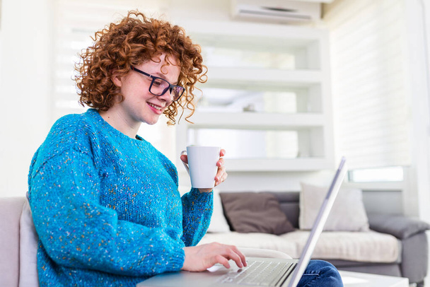 Pozitivní mladá žena na volné noze sledování videa v blogu na netbooku a mají kávu v pohodlném domě. Krásná mladá obchodní žena pracující na laptop.Freelancer připojení k internetu - Fotografie, Obrázek