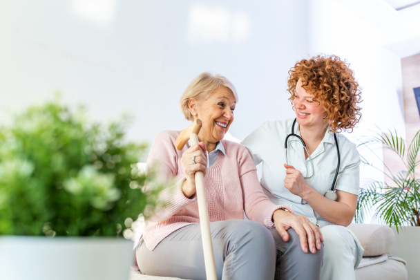 Friendly relationship between smiling caregiver in uniform and happy elderly woman. Supportive young nurse looking at senior woman. Young caring lovely caregiver and happy ward - Photo, Image