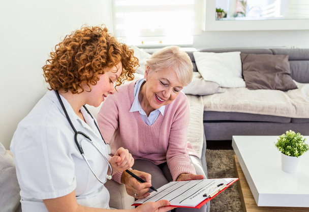 Senior woman is visited by her doctor or caregiver. Female doctor or nurse talking with senior patient. Medicine, age, health care and home care concept. Senior woman with her caregiver at home - Photo, image