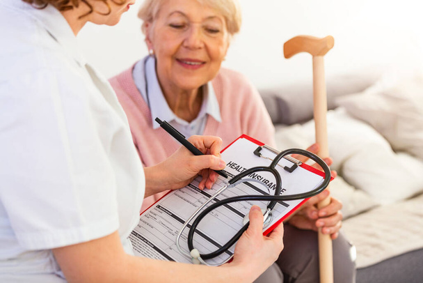 Senior woman is visited by her doctor or caregiver. Female doctor or nurse talking with senior patient. Medicine, age, health care and home care concept. Senior woman with her caregiver at home - Foto, imagen