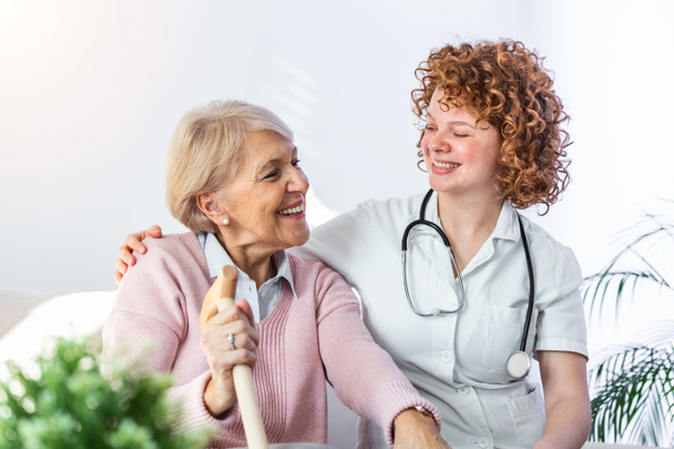Freundliches Verhältnis zwischen einer lächelnden Pflegerin in Uniform und einer glücklichen älteren Frau. Unterstützende junge Krankenschwester schaut Seniorin an. Junge fürsorgliche Pflegekraft und glückliche Station - Foto, Bild