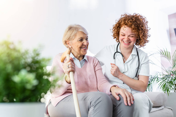 Friendly relationship between smiling caregiver in uniform and happy elderly woman. Supportive young nurse looking at senior woman. Young caring lovely caregiver and happy ward - Foto, immagini