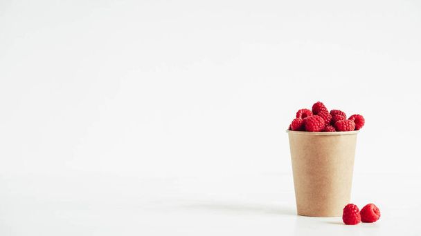 Frambuesas rojas frescas en una taza de papel sobre un fondo de mesa blanco. - Foto, Imagen