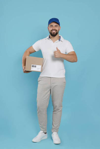 Courier holding cardboard box on light blue background - Foto, Imagen