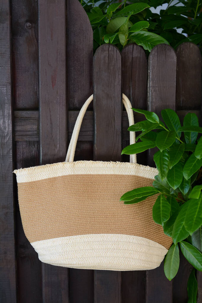 Stylish bag hanging on wooden fence outdoors. Beach accessory - Photo, Image