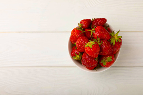 Φρέσκες ώριμες φράουλες σε ένα πιάτο σε ένα λευκό ξύλινο φόντο.Χορτοφαγικά βιολογικά μούρα Υγιεινά τρόφιμα.Βιταμίνες.Copy space.Space για κείμενο - Φωτογραφία, εικόνα