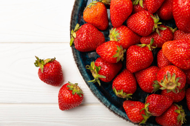 Φρέσκες ώριμες φράουλες σε ένα πιάτο σε ένα λευκό ξύλινο φόντο.Χορτοφαγικά βιολογικά μούρα Υγιεινά τρόφιμα.Βιταμίνες.Copy space.Space για κείμενο - Φωτογραφία, εικόνα