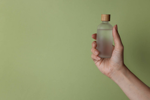 Woman holding bottle of cosmetic product on pale olive background, closeup. Space for text - Fotoğraf, Görsel