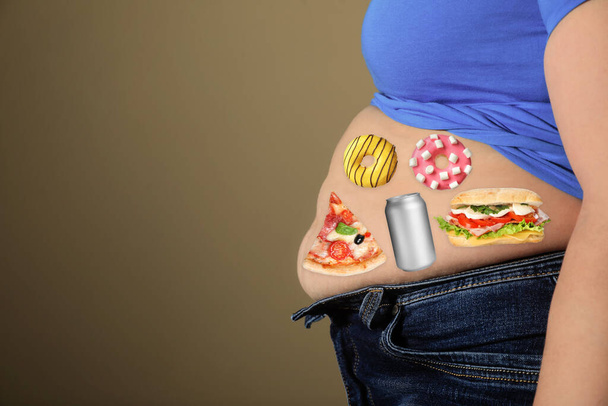 Overweight woman in tight shirt and jeans with images of different unhealthy food on her belly against light brown background, closeup. Space for text - Foto, afbeelding