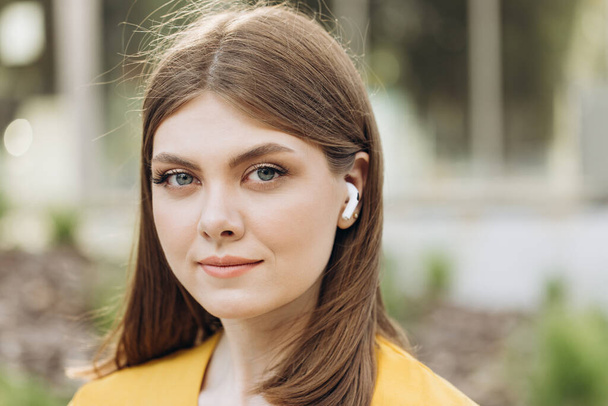 Face of pretty young girl in wireless earphones outside. Woman with wireless earphones on her ears. - Photo, image