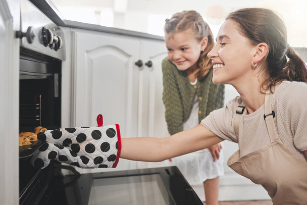 Foto de una madre y una hija poniendo una bandeja de galletas en el horno en casa. - Foto, imagen