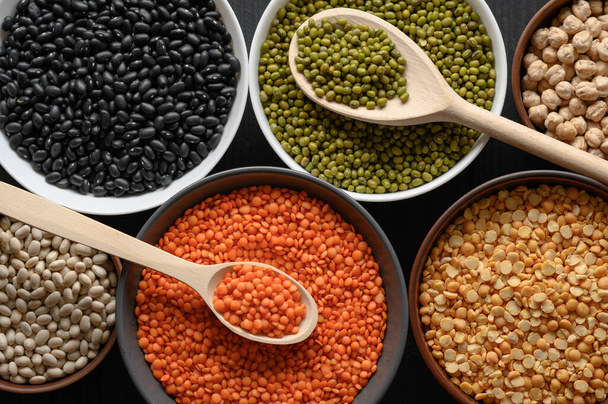 Overhead view of bowls of assorted raw legumes on a dark wooden table - Photo, Image