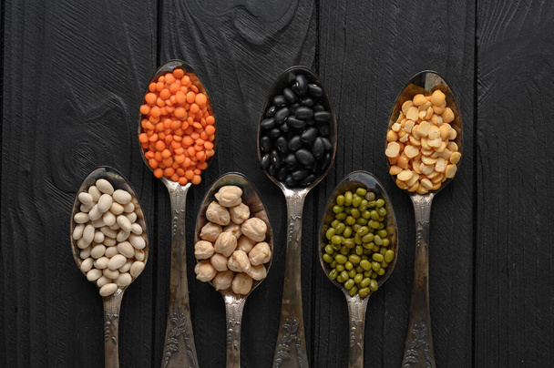Variedade de legumes em colheres de prata velhas em um fundo de madeira preta. - Foto, Imagem