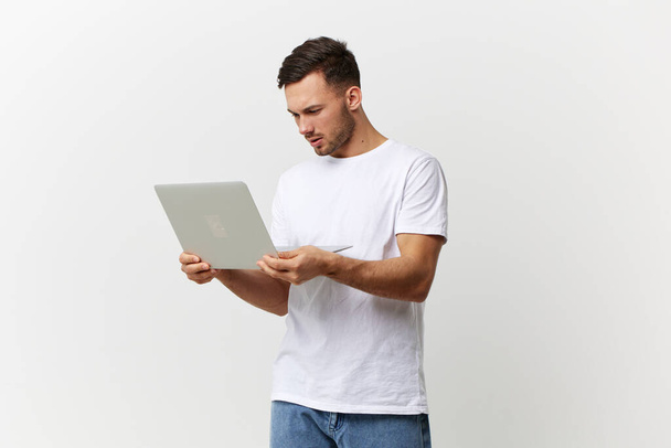 Unglücklich wütend braungebrannte gutaussehende Männer im einfachen T-Shirt haben ein Problem mit kaputtem Laptop, der isoliert auf weißem Studiohintergrund posiert. Kopierraum Banner-Attrappe. Elektronik repariert IT-Konzept - Foto, Bild