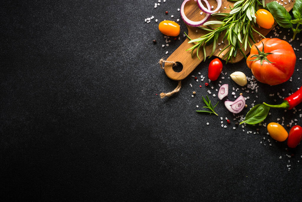 Yemek pişirme arka planı siyah taş masada. Taze sebzeler, otlar ve baharatlar. Kopyalama alanı olan üst görünüm. - Fotoğraf, Görsel
