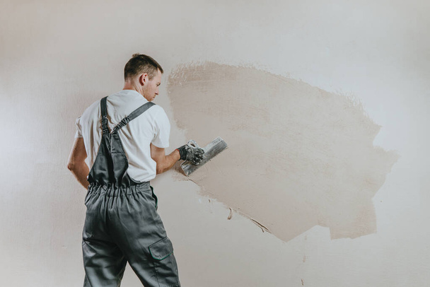 Férfi munkaruhás munkás overál vakolat egy fal egy építési vakolat. Vízszintes panoráma banner üres szövegrésszel. - Fotó, kép