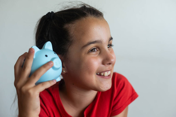 Little girl saving money in a piggybank over a white background. - Photo, Image