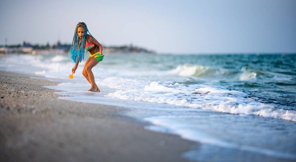 Funny slender cheerful girl playing with small waves, kicking their feet and spinning in place under the warm bright summer sun enjoying the long-awaited vacation - Fotoğraf, Görsel