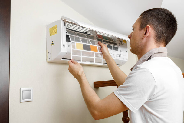 Male technician cleaning air conditioner indoors. - Φωτογραφία, εικόνα