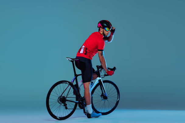 Training. Studio shot of professional cyclist in red sports uniform, goggles and a helmet on a blue background. Concept of active life, rest, travel, energy, sport. Copy space for ad - Fotografie, Obrázek