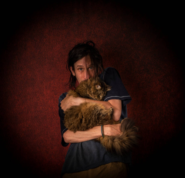 Uomo drogato con giovane gatto tabby con grandi occhi verdi vicino al muro rosso - Foto, immagini