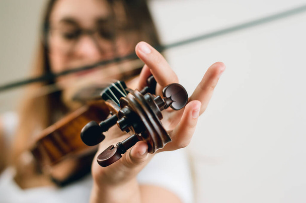 blurred woman violinist tuning violin, focus on hand and peg, copy space on right. concept of music and music education. - Фото, зображення
